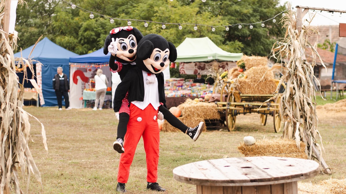 Festival scene with two people in mouse character costumes enjoying an autumn fair outdoors.